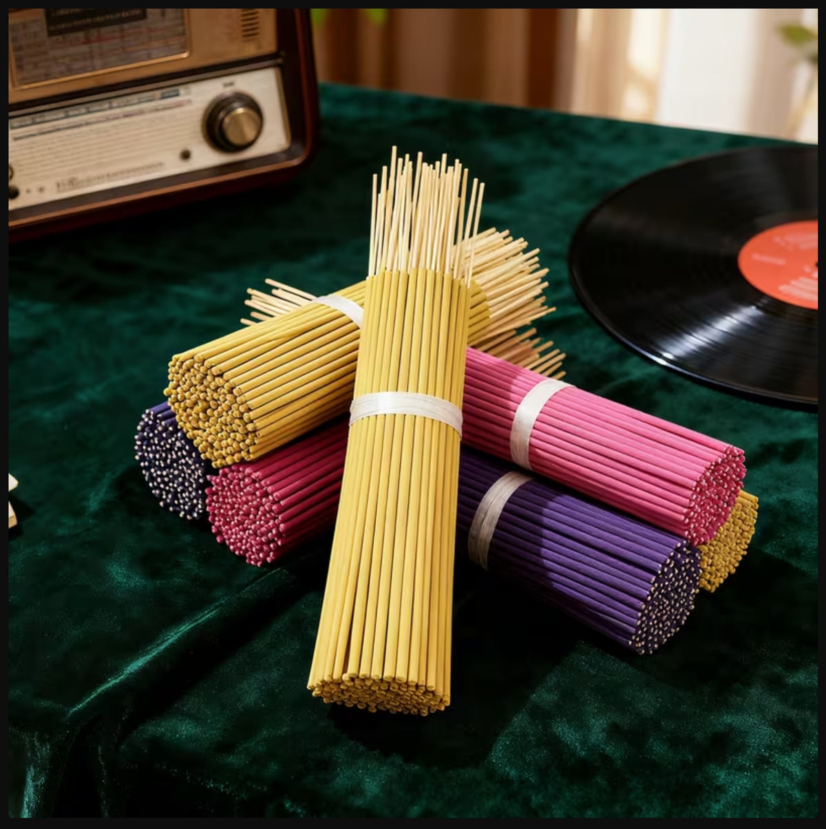 Four bundles of incense sticks tied with white bands, displayed on a dark green velvet surface. The incense sticks are in multiple colors: yellow, pink, purple, and dark red.