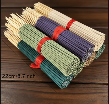 Three bundled sticks of chopsticks tied with red ribbons, shown on a dark wood surface. The front bundle is teal, the middle bundle is light green, and the back bundle is lavender.