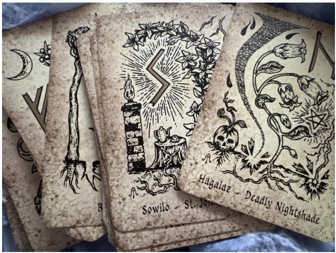 A stack of tarot cards with vintage-style black illustrations and text on aged, yellowed cardstock, photographed close up against a blue fabric background.